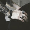 Le bras et la main d'une personne ornés de tatouages, de bracelets de perles noires et de deux bagues en argent.