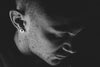 Un visage d'homme en noir et blanc, avec un piercings à l'oreille.