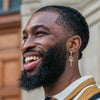 Un homme souriant avec une barbe et des cheveux tressés portant une boucle d'oreille en ankh.