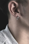 Une boucle d'oreille en argent avec un design à double bande, portée sur l'oreille d'une personne.