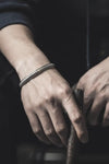 Les mains d'une personne portant un bracelet en argent texturé et tenant un objet sombre et texturé.